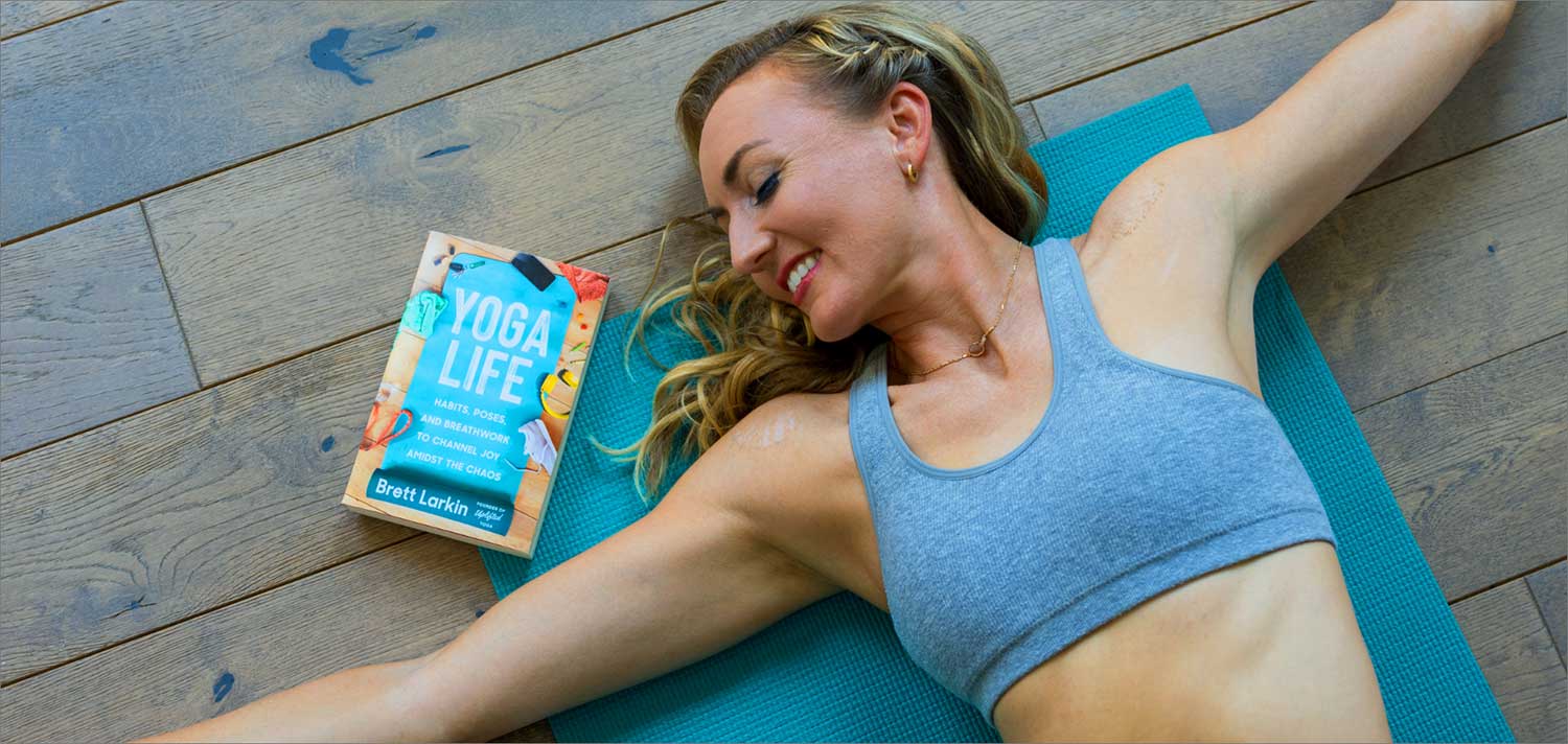 Yoga teacher lying in a supine twist next to the Yoga Life book